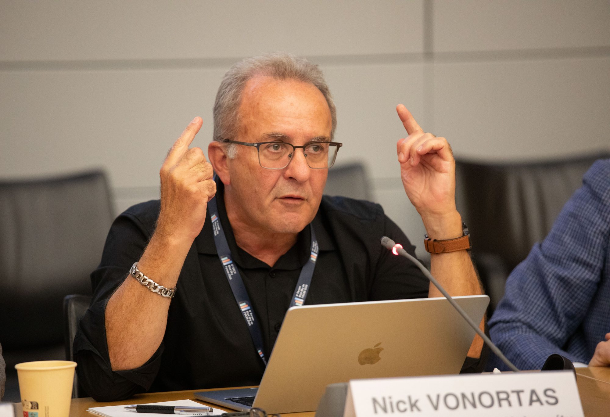 Nick Vonortas speaking at a conference table, with a name card in front of him